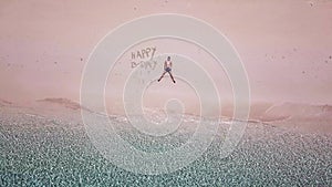 A drone shot of a man lying on a pink sand beach next to `Happy Birthday` sign on a small island near Maumere, Indonesia. Happy