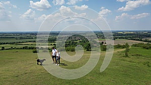 Drone Shot Of Mature Couple Walking With Pet Dog Through Beautiful English Countryside