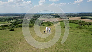 Drone Shot Of Mature Couple Walking With Pet Dog Through Beautiful English Countryside