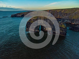 Drone shot of naturally formatted rocky cliffs in the sea under blue cloudy sky at sunset