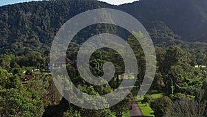 Drone shot over green trees and road, hills and mountain