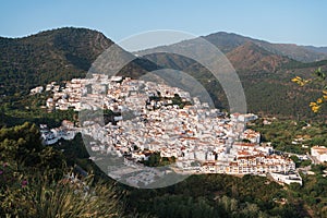 Drone shot over Ojen, Spain showcasing the white buildings nestled in the green hills of Andalusia