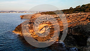 Drone shot of the rugged cliffs at Sa Coma beach in Mallorca, Spain, during a stunning sunset