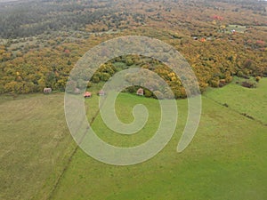 Drone shot of rural wooden cottages in a large green field in Sjenica, Serbia photo