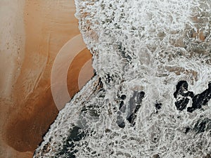 Drone shot of water waves crashing sandy beach