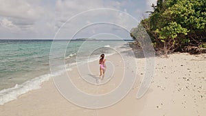 Drone shot of woman running on Maldives beach, waves and trees