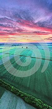 Drone vertical panorama view from above of a field, agriculture land. Sun with clouds at sunset