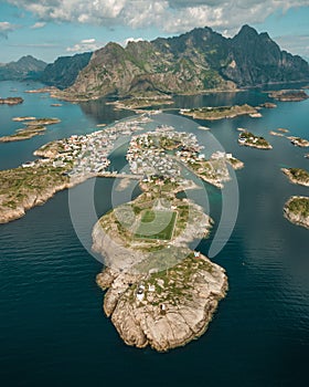 Drone vertical shot over houses with football pitch in an island with mountain in the background