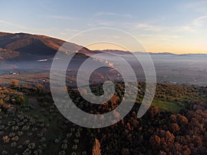 Drone view of Assisi Umbria Italy above mist at sunset with autumn trees in the foreground