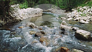 Drone view captures mountain river, stone lined banks in forest. Clear water flows over stones in mountain river