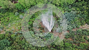 Drone view captures pipe, spraying water in green mountain canyon. Aerial footage shows pipe, spraying fountain due to