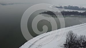 Drone view of coasts with leafless trees covered in snow by a lake