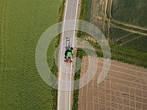 Drone view of a green tractor on asphalt road between agriculture fields