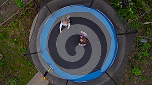 Drone view of jumping girls from above. Little girls jump on a trampoline in the yard. The camera is spinning.