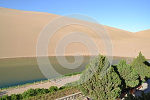 Drone view of the Mingsha Mountain and Crescent Moon spring surrounded by trees in Jiuquan, China