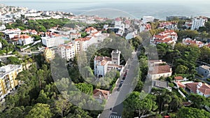 Drone view of Monte Estoril, Portugal with buildings, a road, trees and the ocean in the background.