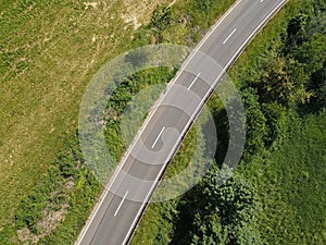 Drone view of a road with white stripes between grass and trees in the landscape in summer