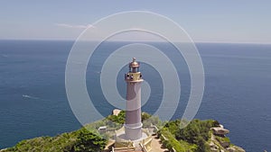 Drone view sea lighthouse on mountain cliff and sailing ships. Aerial landscape lighthouse on green mountain and boat