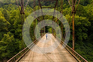 Drone view of senior woman walking dog across Jenkinsburg Bridge over Cheat River