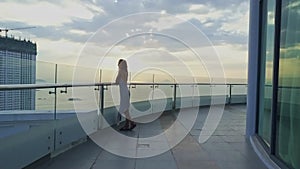 Drone view slim girl stands on hotel top floor against sunrise