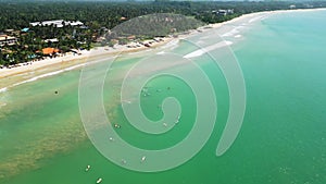 Drone view of surfers in turquoise sea at tropical beach. Aerial shot captures crowd of people with surfboards waiting