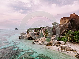 Drone view at the white beach with happy Young couple walking on the beach by the ocean with palmtrees at the Seychelles