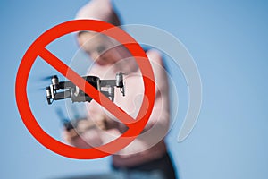 Drones are prohibited. Four-propeller drone flying in nature against sky and operator. Enclosed in red prohibition sign.