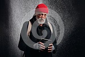 Drooping old beggar man in street clothes stand in heavy rain