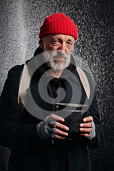 Drooping old beggar man in street clothes stand in heavy rain