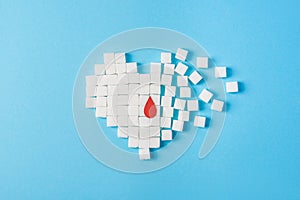 A drop of blood on broken heart made of pure white cubes of sugar isolated on blue background, World diabetes day