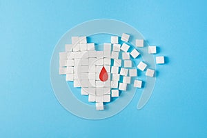 A drop of blood on broken heart made of pure white cubes of sugar isolated on blue background, World diabetes day photo