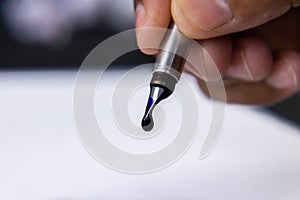Drop of blue ink dripping out from a fountain pen nib over white paper