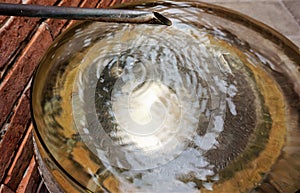 A drop of clear water dripping into a golden metal basin