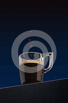 Drop of coffee falls into a transparent glass coffee cup