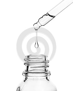 A drop falls into a glass bottle. Cosmetic oil dripping from a pipette on a white background