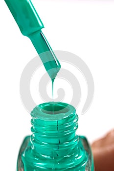 Drop of green nail Polish on a brush over an open bottle.