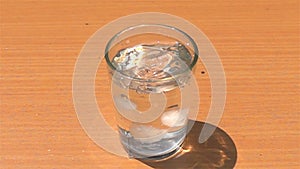 Drop homemade ice cubes into a glass filled with fresh water on a wooden table