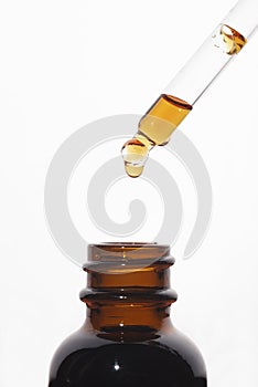 A drop of liquid falling from a pipette into an amber bottle. Skincare products, natural cosmetic on white background.