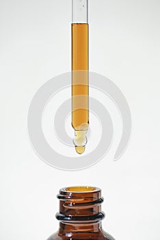 A drop of liquid falling from a pipette into an amber bottle. Skincare products, natural cosmetic on white background.