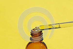 A drop of liquid falling from a pipette into an amber bottle. Skincare products, natural cosmetic on yellow background.