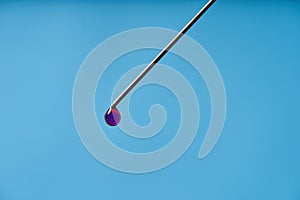 A drop of medicine on the tip of a medical injection needle. Blue background