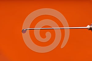 A drop of medicine on the tip of a medical injection needle. Red background