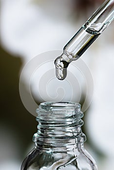 Drop of oil on a background of flowers. Cosmetic pipette with essence