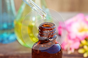 Drop of oil dripping from pipette into bottles of essential oil