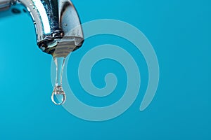 Drop of water coming out of water tap on blue background with copy sapce photo