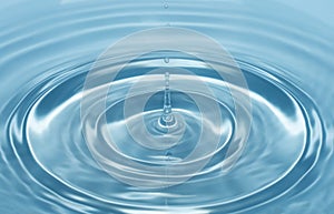 A drop of water falls with a splash into clear, blue water forming circles on the water