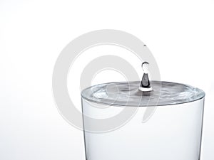 Drop of water, about to make the glass overflow and run over. On white.