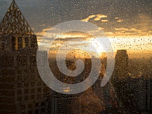 Drop of water on widow glass with light sunset in city and building view. Rainy season feeling alone. Work in city life concept