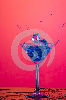 Droplets of Drink Spilling Out of The Glass Goblet with Icecubes and Colorful Liquid. Isolated Over Colorful Background
