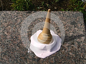 Dropped ice-cream cone melting on ground in summertime